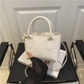 Mini white litchi pattern leather handbag with adjustable crossbody strap on a chair - White