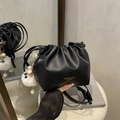Black pleated bucket bag with gold logo and cute white plush charm on a white stool - Black With Pendant