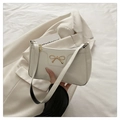 Close-up of white patent leather shoulder bag featuring a gold metal bow ornament - White