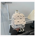 Close-up of beige corduroy mini backpack with black quilted bow pattern and front pocket - Off White