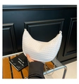 White woven crescent bag with gold chain strap held by a model in a modern studio - White