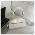 Creamy white Boston style crossbody pillow bag with gold hardware on a white sofa - White