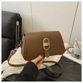 Brown leather crossbody bag with gold D-buckle shown against a minimalist home background - Brown