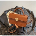 Détail d'un sac à main marron motif crocodile avec boucle dorée sur veste noire - Marron