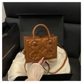 Close-up of caramel brown handbag with embossed floral pattern and gold metal hardware - Brown