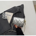 Detalle de bolso acolchado plateado con esfera dorada sobre fondo de traje gris - Plateado