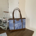 Chic blue denim tote bag with brown leather trim for commuting, shown on wooden table - Blue