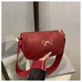 Detalle de bolso cilíndrico rojo con lazo dorado y correa ancha de tela ajustable - Rojo