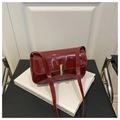 Glossy red patent leather shoulder bag with gold metal buckle on white books background - Red
