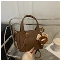 Close-up of brown litchi pattern leather bucket bag with plush monster charm and gold hardware - Brown with Pendant