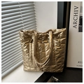 Primer plano del bolso tote acolchado dorado con textura metálica y bolsillo frontal - Dorado