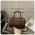 Detail van donkerbruine leren crossbodytas met letteropdruk en zilveren metalen hardware - koffiekleur