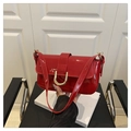 Detail of red patent leather shoulder bag with gold metal clasp on a black chair - Red
