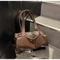 Close-up of a glossy dark brown baguette bag on a book with polished oil-wax texture - Coffee