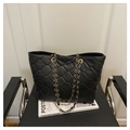 Detailansicht der schwarzen gesteppten Handtasche mit goldener Kette auf einem Stuhl - Schwarz