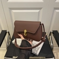 Minimalist brown leather shoulder bag with gold clasp and knotted strap on a chair - Brown