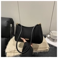 Dettaglio borsa sottobraccio nera con finiture dorate su un tavolino da caffè accogliente - Nero
