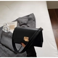 Vista detallada del bolso bandolera negro minimalista con cierre dorado sobre una chaqueta - Negro