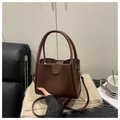 Detalle de bolso tipo cubo vintage en cuero PU marrón sobre punto beige con asa y correa - café