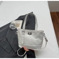 Detail der weißen Leder-Mini-Tote mit silbernem Drehverschluss auf neutralem Hintergrund - Gebrochenes Weiß