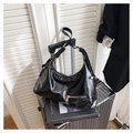 Detail of black patent leather hobo bag with gold hardware on a silver suitcase - Black