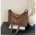 Detail view of large brown suede crossbody bag styled with book and minimalist vase - Coffee
