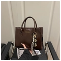 Detail view of deep brown glossy tote bag with gold lettering and woven chain charm - Coffee