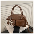 Detail of a shiny brown Boston bag featuring pearl bow charm and twin front pockets - Brown