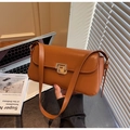 Detail der braunen Retro-Baguette-Tasche mit goldenem Schloss auf minimalistischem Tisch - Braun
