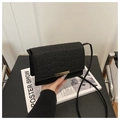 Black crocodile pattern crossbody bag with golden buckle on a fashion magazine - Black
