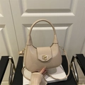 Glossy beige crescent handbag with gold twist lock and shoulder strap on leather chair - Khaki
