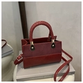Burgundy contrast handbag with woven handle and gold hardware on grey books - Red