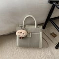 Detail view of two-tone crossbody bag with plush charm on a textured carpet background - White