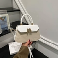 Close-up of woven straw handbag with white leather flap and golden M-letter buckle - White