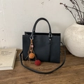 Detalle de bolso negro texturizado con colgante de peluche sobre superficie madera - Con Colgante / Negro