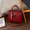 Rode crossbodytas met visgraatmotief, gouden letters en kralenkwastje op houten vloer - Met Hanger / Rood