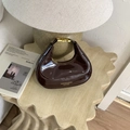 Detalle de un bolso hobo de charol marrón oscuro brillante sobre una mesa de madera artística - Marrón