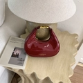 Detalle de bolso medialuna de charol rojo con cierre dorado sobre mesa - Rojo