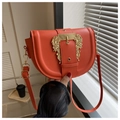 Macro shot of orange saddle bag with large gold baroque buckle and matte leather texture - Orange