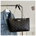 Detail of black quilted tote bag with gold chain strap next to denim jacket - Black