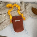 Corduroy crossbody bag with yellow ruffled strap and drawstring in a lifestyle setting - Brown