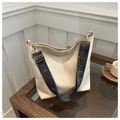 Dettaglio della borsa a secchiello beige con tracolla ricamata su tavolo in legno - Cachi