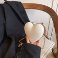 Detailed macro view of heart-shaped white clutch with elegant gold frame and metal snap closure - White