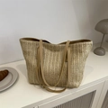 Beige geflochtene Tragetasche mit braunen Griffen auf einem modernen weißen Schrank - Khaki