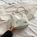 White bucket bag with silver butterfly charms and chain strap in a cozy home setting - White