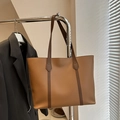 Minimalistische warm bruine lederen tote bag met donkere hengsels in een zakelijke kantooromgeving - Tan