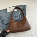 Borsa hobo marrone con trama intrecciata sopra jeans e una rivista d'arte - Marrone