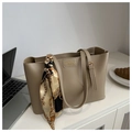 Detalle del bolso tote de cuero beige con placa dorada y pañuelo de seda en un escritorio - Caqui