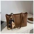 Detalle de un bolso tote de cuero marrón con logo grabado y un pañuelo de seda vintage - Tostado