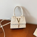 Weiße gesteppte Handtasche mit goldenem V-Logo und Quastenanhänger auf Holzoberfläche - Weiß